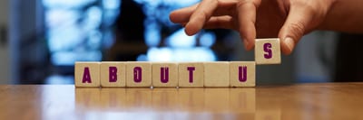 Hand som placerar bokstavsklossar som tillsammans bildar ordet ”ABOUT US”.